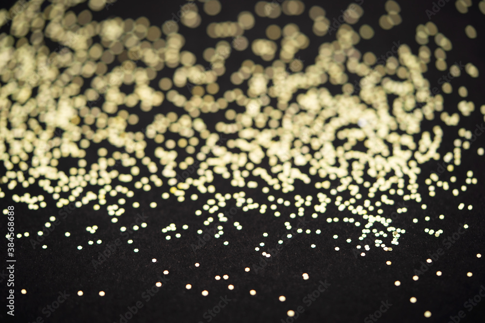 Beautiful Christmas light background. Abstract glitter bokeh and scattered sparkles in gold, on black