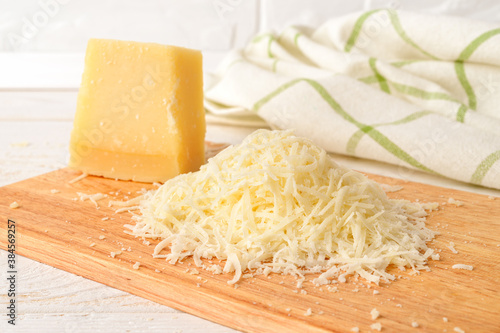 Heap of grated italian hard cheese Grana Padano or Parmesan on a wood cutting board over white wood table. Delicious ingredient for pizza, sandwiches, salads.