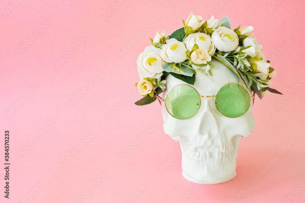 Human skull with green glasses and flowers on white background