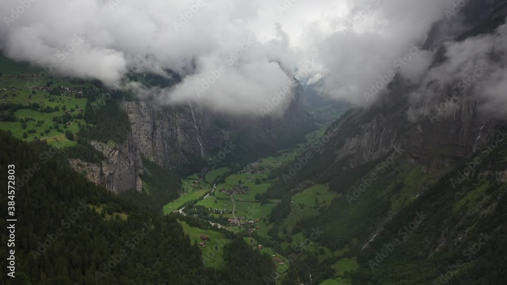 Drone shot moving forward over the epic valley and village Lauterbrunnen in the alps of Switzerland. Dramatic and epic clouds moving in over the valley with beautiful lush green fields on the sides. Drone shot moving forward over the epic valley and village Lauterbrunnen in the alps of Switzerland. Dramatic and epic clouds moving in over the valley with beautiful lush green fields on the sides.
