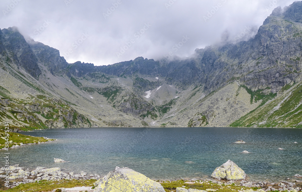 The largest mountain lake on slovakian side of High Tatras, Hincovo pleso in Mengusovska valley surrounded by rocky mountains under low clouds