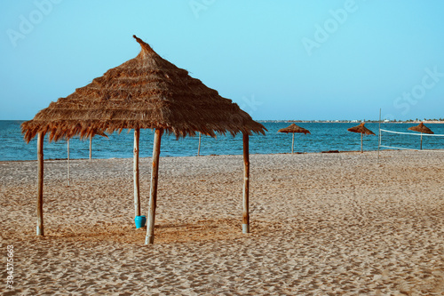 Fototapeta Naklejka Na Ścianę i Meble -  A beach by the sea with straw umbrellas on the sand.
