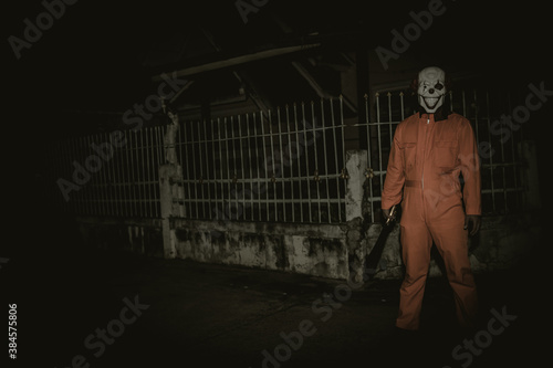 Asian handsome man wear clown mask with weapon at the night scene,Halloween festival concept,Horror scary photo of a killer in orange cloth