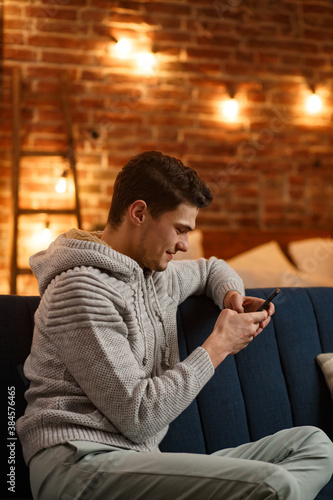 Young freelancer using smartphone and smiling. Happy man using mobile phone apps, texting message, browsing internet, looking at smartphone, sitting at home. Young people working with mobile devices.