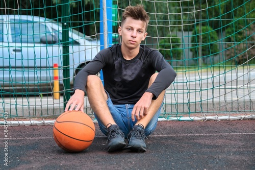 Outdoor portrait of teenage boy with ball on street basketball court © Valerii Honcharuk