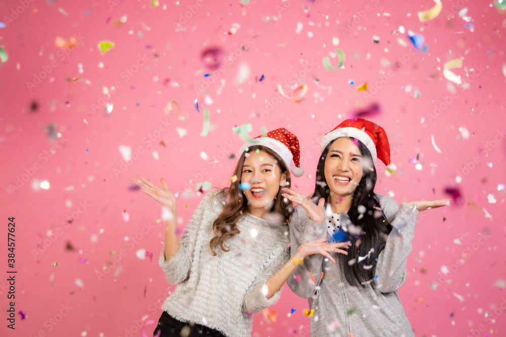 Portrait of two lovely cute asian women in christmas hats  looking at camera isolated over pink background.Attractive asian woman smile in christmas, new year, valentine day, birthday .