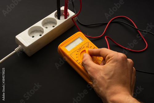 Measuring the current in the socket, extension cable using multimeter. Person turns on  multimeter. Multimeter terminals is connected to outlet