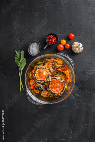 Mushrooms,baked and stuffed with ingredients cheddar cheese, cherry tomatoes and sage in glass pot on black background top view.