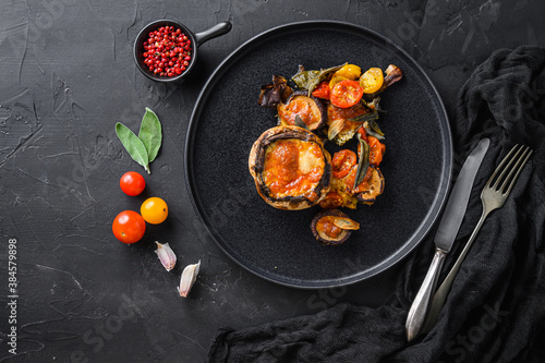 Served portobello mushrooms,baked and stuffed with ingredients cheddar cheese, cherry tomatoes and sage on black plate over black background top view space for text.
