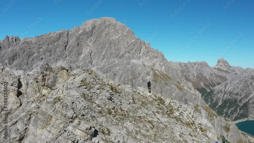 A man is standing by himself alone on top of Lunersee mountain in Switzerland. Big rocks and boulders make up the hill around the heart shaped lake during a sunny clear day. A man is standing by himself alone on top of Lunersee mountain in Switzerland. Big rocks and boulders make up the hill around the heart shaped lake during a sunny clear day.