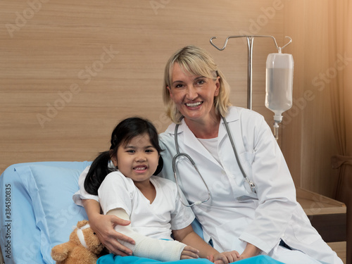 Caucasian peditrician or Orthopedic doctor checking the broken arm of cute Asian girl. photo