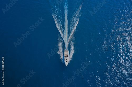 Drone view of a boat  the blue clear waters. Top view of a white boat sailing to the blue sea. Large speed boat moving at high speed. Travel - image.