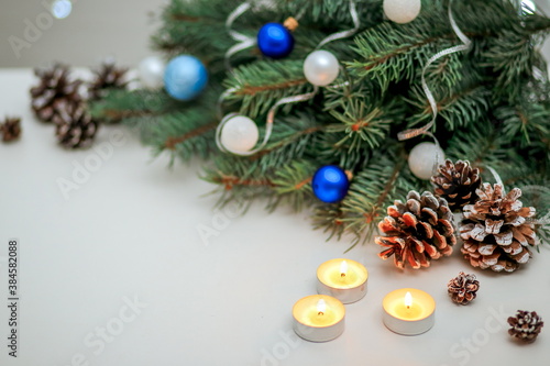 Christmas composition with fir branches, Christmas toys and burning candles, greeting card on the background of a bokeh of lights garland
