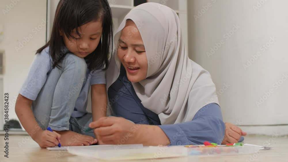Asian muslim mother drawing with her daughter, single mom teaching baby girl, learning on the floor, happy family