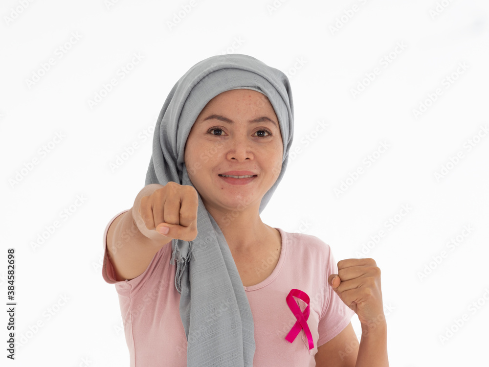 Breast Cancer Awareness month. Asian woman with headscarf and pink ribbon on the chest, putting fist in front gesture like fighting for illness. Breast Cancer Awareness month. Asian woman with headscarf and pink ribbon on the chest, putting fist in front gesture like fighting for illness.