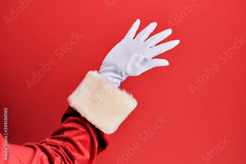 Hand of a man wearing santa claus costume and gloves over red background presenting with open palm, reaching for support and help, assistance gesture