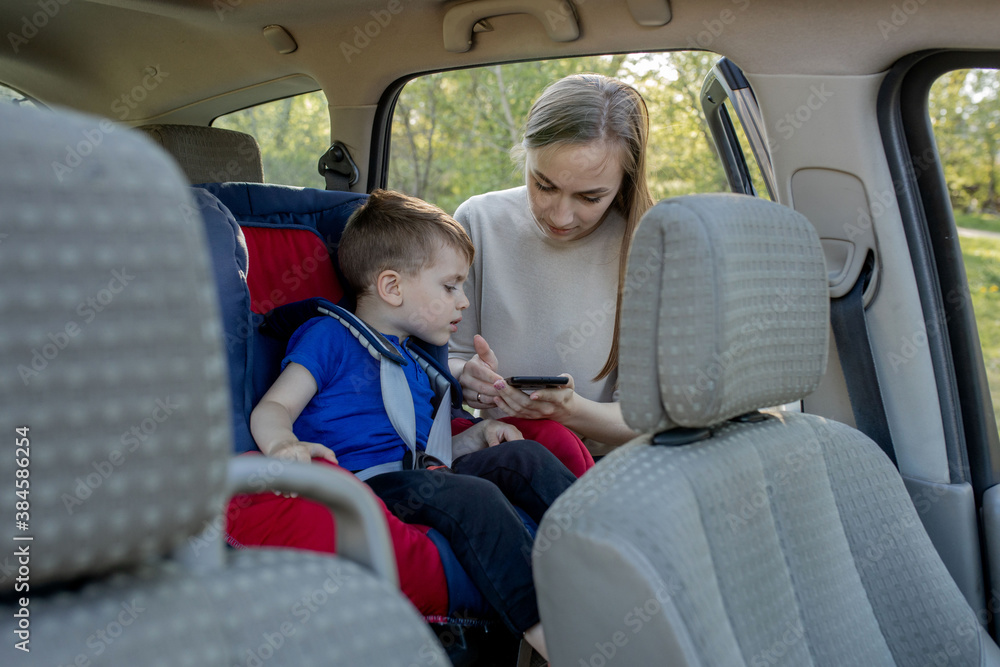Mother gives the phone little boy sitting in a car seat. Safety of transportation of children. Mother gives the phone little boy sitting in a car seat. Safety of transportation of children.