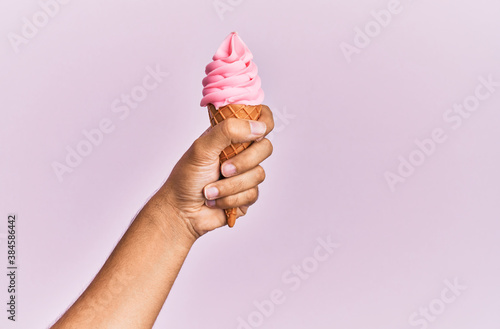 Hand of hispanic man holding ice cream over isolated pink background. photo