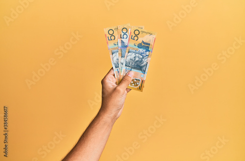Hand of hispanic man holding australian 50 dollars banknotes over isolated yellow background.