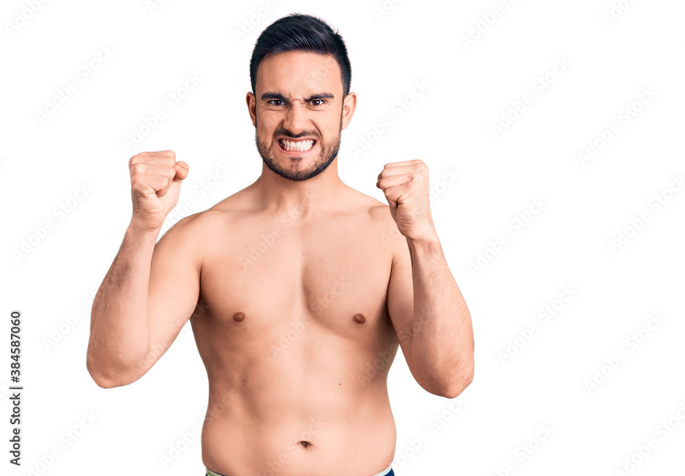 Fototapeta premium Young handsome man wearing swimwear angry and mad raising fists frustrated and furious while shouting with anger. rage and aggressive concept.