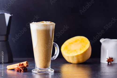 Pumpkin spice latte, coffee maker and milk jug on a dark background. Pumpkin latte with whipped cream and piece of pumpkin. Hot autumn drink