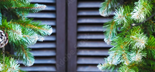 Christmas window. Shutters on the window, panoramic view. Garland of green fir branches and cones, luminous xmas garland, frame