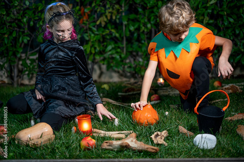 Little girl and boy in witch costume on Halloween trick or treat in the night garden. Children celebrate Halloween at decorated fireplace. Concept of children ready for a party. © Elena