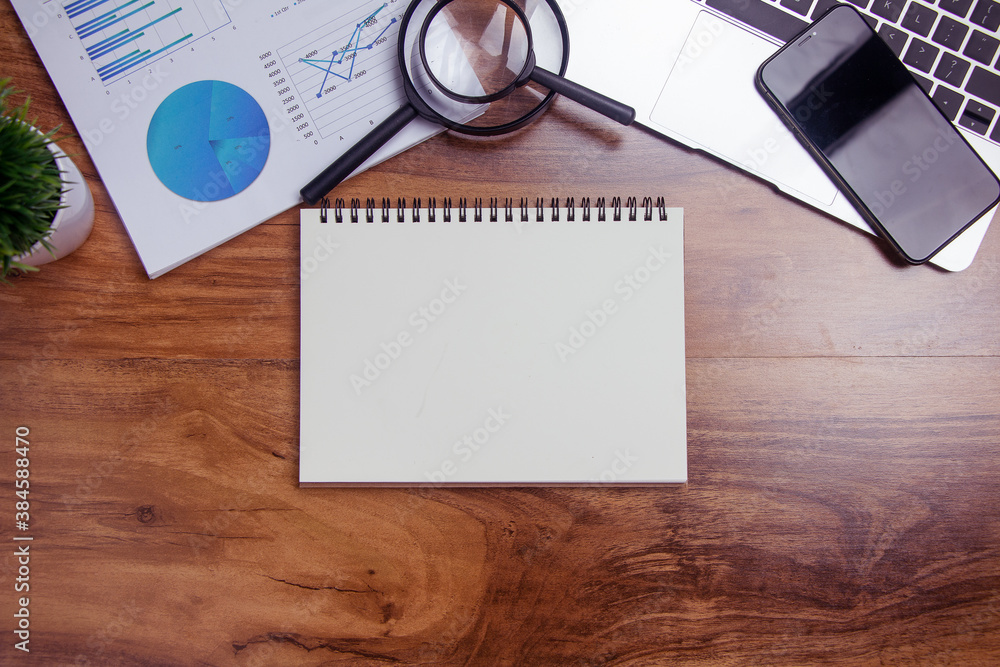 Top view,Business desk with a notebook, report graph chart, pen and tablet on wooden table Top view,Business desk with a notebook, report graph chart, pen and tablet on wooden table