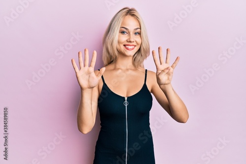 Beautiful caucasian blonde girl wearing sexy party dress showing and pointing up with fingers number nine while smiling confident and happy.