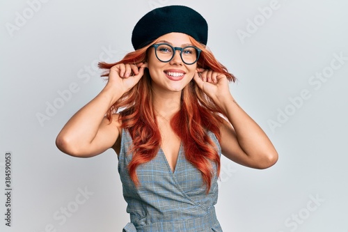 Young redhead woman wearing fashion french look with beret smiling pulling ears with fingers, funny gesture. audition problem