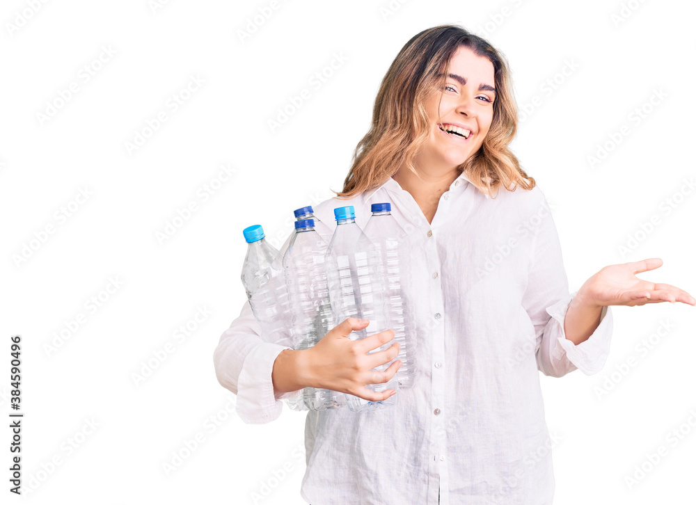 Young caucasian woman holding recycling plastic bottles celebrating victory with happy smile and winner expression with raised hands Young caucasian woman holding recycling plastic bottles celebrating victory with happy smile and winner expression with raised hands
