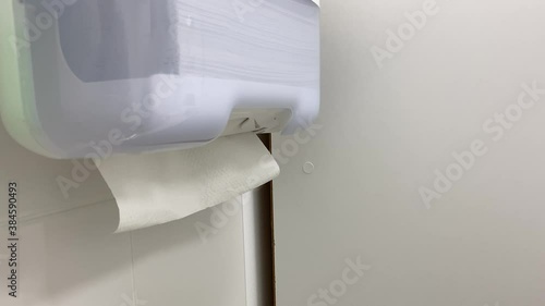 Close up of nurse hands pulling tissues from white plastic box in clinic. White paper towel dispenser on the wall. Health care and prevention concept.