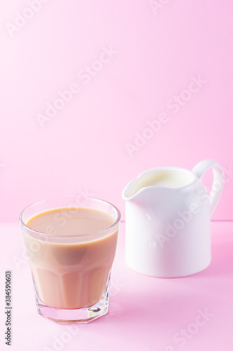 Milk tea on a pink background. Glass of masala chai tea and milk jug. Spiced tea and milk on a pastel background. Minimalism. Copy space