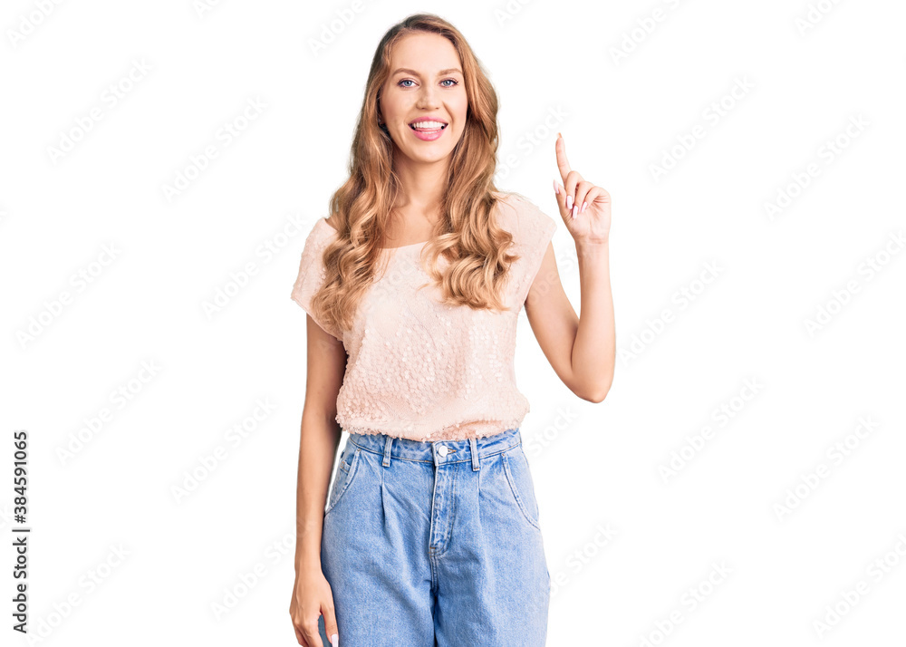 Young beautiful caucasian woman with blond hair wearing casual clothes showing and pointing up with finger number one while smiling confident and happy. Young beautiful caucasian woman with blond hair wearing casual clothes showing and pointing up with finger number one while smiling confident and happy.