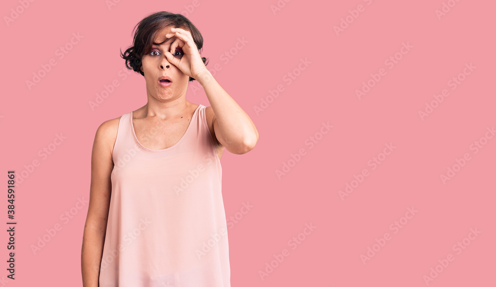 Beautiful young woman with short hair wearing casual style with sleeveless shirt doing ok gesture shocked with surprised face, eye looking through fingers. unbelieving expression.