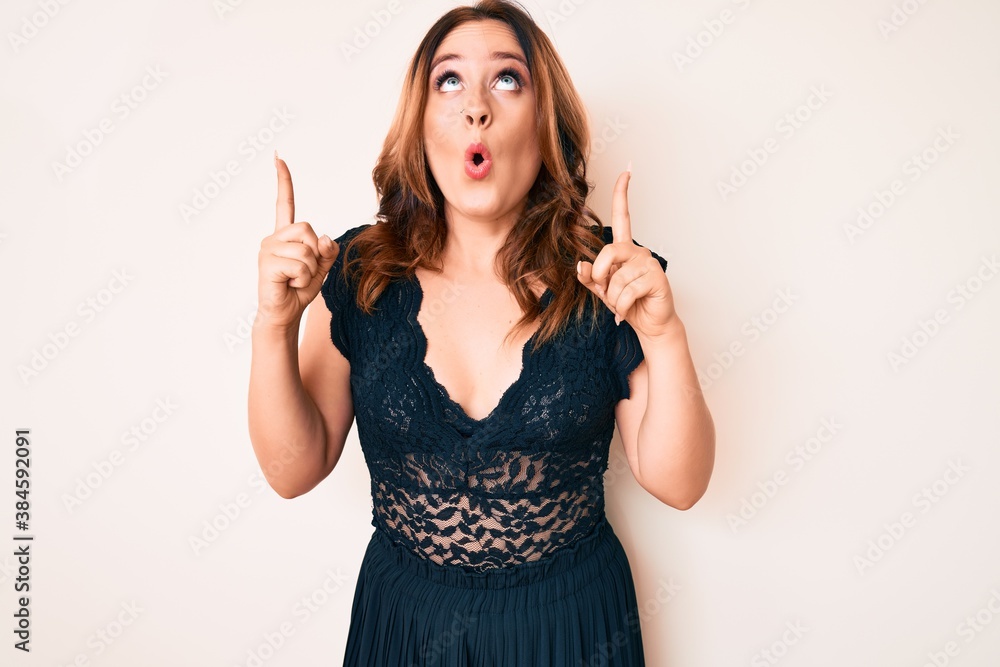 Young beautiful caucasian woman wearing elegant clothes amazed and surprised looking up and pointing with fingers and raised arms. Young beautiful caucasian woman wearing elegant clothes amazed and surprised looking up and pointing with fingers and raised arms.