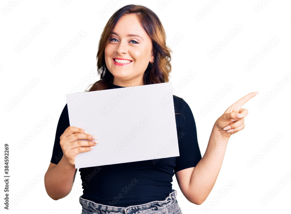 Young beautiful caucasian woman holding blank empty paper smiling happy pointing with hand and finger to the side Young beautiful caucasian woman holding blank empty paper smiling happy pointing with hand and finger to the side