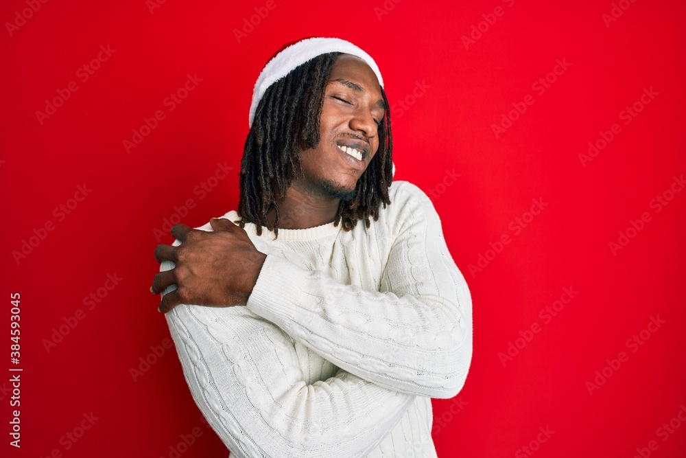 African american man with braids wearing christmas hat hugging oneself happy and positive, smiling confident. self love and self care African american man with braids wearing christmas hat hugging oneself happy and positive, smiling confident. self love and self care