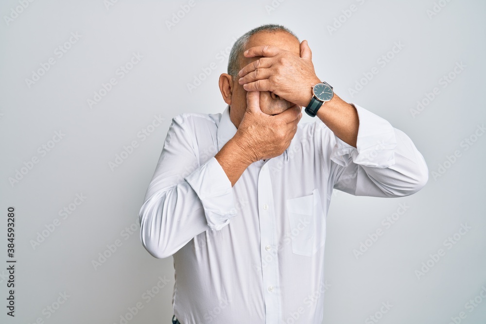 Handsome senior man wearing casual white shirt covering eyes and mouth with hands, surprised and shocked. hiding emotion Handsome senior man wearing casual white shirt covering eyes and mouth with hands, surprised and shocked. hiding emotion