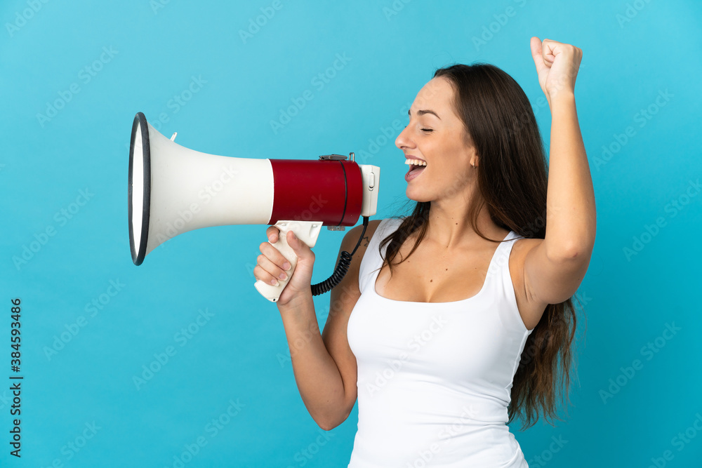 Young hispanic woman over isolated blue background shouting through a megaphone to announce something in lateral position Young hispanic woman over isolated blue background shouting through a megaphone to announce something in lateral position