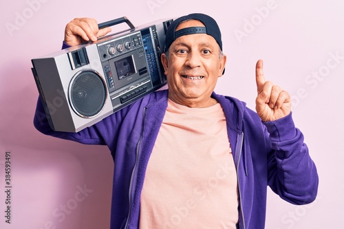 Senior handsome grey-haired modern man listening to music using vintage boombox smiling with an idea or question pointing finger with happy face, number one