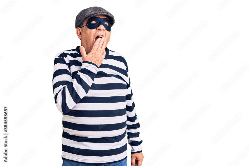 Senior handsome man wearing burglar mask and t-shirt bored yawning tired covering mouth with hand. restless and sleepiness. Senior handsome man wearing burglar mask and t-shirt bored yawning tired covering mouth with hand. restless and sleepiness.