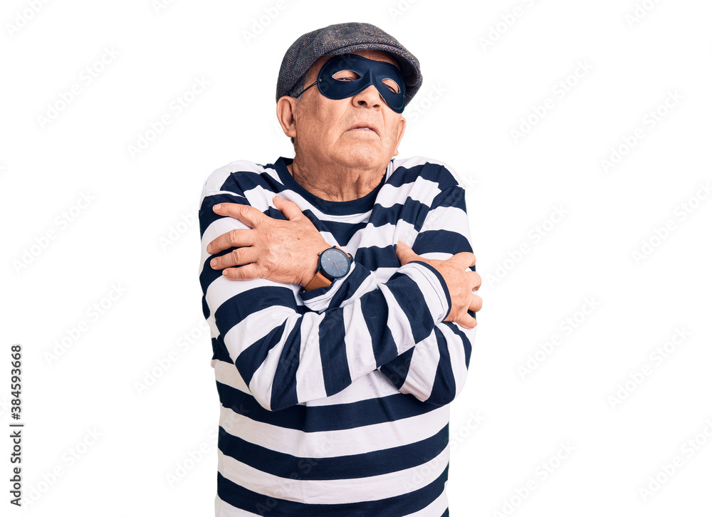 Senior handsome man wearing burglar mask and t-shirt shaking and freezing for winter cold with sad and shock expression on face Senior handsome man wearing burglar mask and t-shirt shaking and freezing for winter cold with sad and shock expression on face