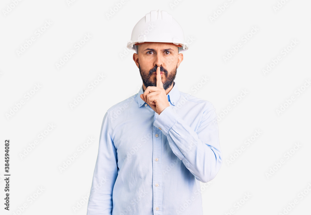 Young handsome man wearing architect hardhat asking to be quiet with finger on lips. silence and secret concept. Young handsome man wearing architect hardhat asking to be quiet with finger on lips. silence and secret concept.