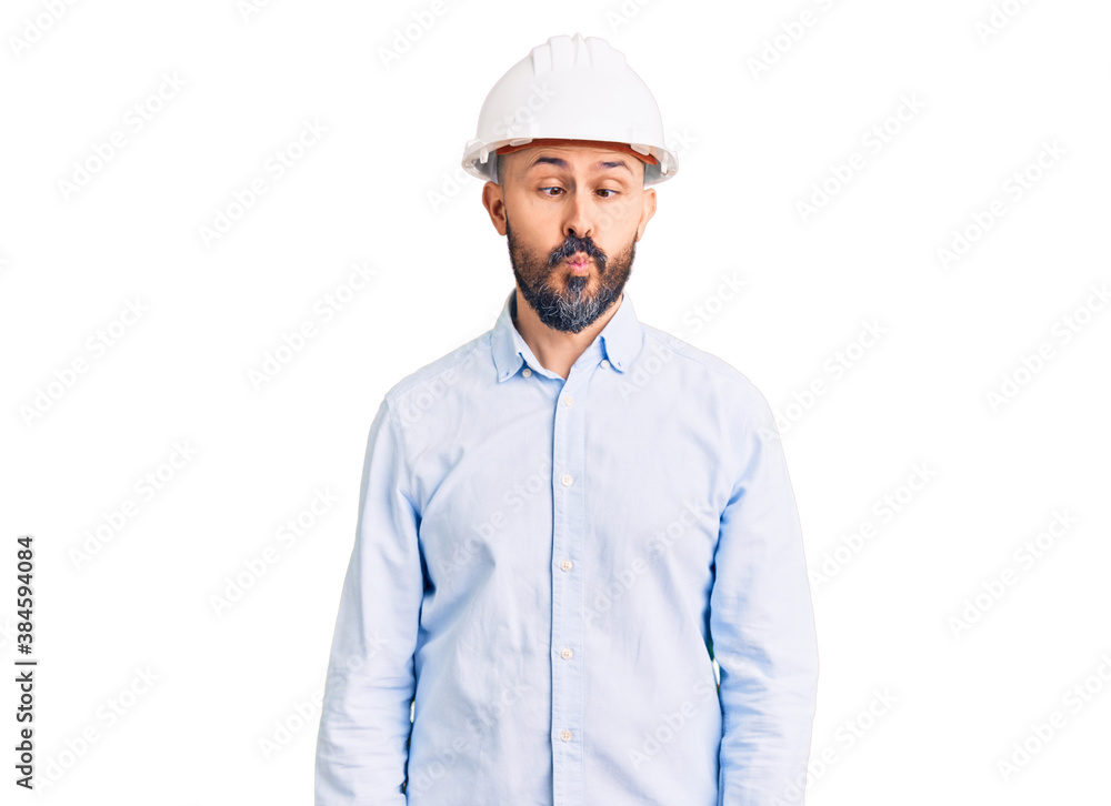 Young handsome man wearing architect hardhat making fish face with lips, crazy and comical gesture. funny expression. Young handsome man wearing architect hardhat making fish face with lips, crazy and comical gesture. funny expression.