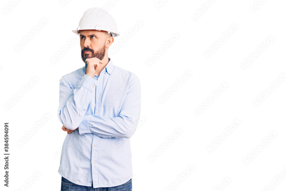 Young handsome man wearing architect hardhat with hand on chin thinking about question, pensive expression. smiling with thoughtful face. doubt concept. Young handsome man wearing architect hardhat with hand on chin thinking about question, pensive expression. smiling with thoughtful face. doubt concept.