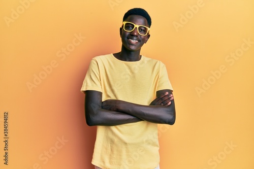 Young african american man wearing casual clothes and glasses happy face smiling with crossed arms looking at the camera. positive person. © Krakenimages.com
