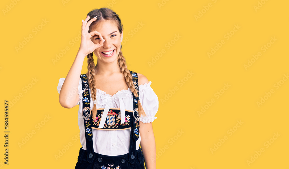 Beautiful caucasian woman with blonde hair wearing octoberfest traditional clothes doing ok gesture with hand smiling, eye looking through fingers with happy face. Beautiful caucasian woman with blonde hair wearing octoberfest traditional clothes doing ok gesture with hand smiling, eye looking through fingers with happy face.