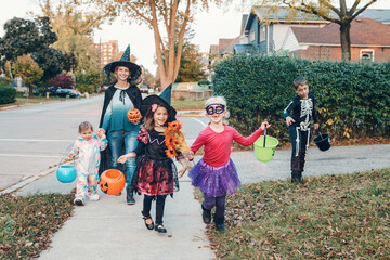 Trick or treat. Mother with children going to trick or treat on Halloween holiday. Mom with kids in party costumes with baskets going to neighbourhood homes for candies, treats.