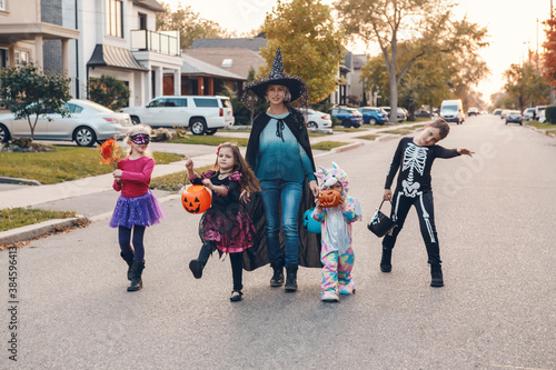 Trick or treat. Mother with children going to trick or treat on Halloween holiday. Mom with kids in party costumes with baskets going to neighbourhood homes for candies, treats.